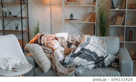 Home flu. Mobile communication. Headache suffer. Unhealthy sick woman influenza symptoms calling doctor feeling bad lying on couch home interior. 104131428