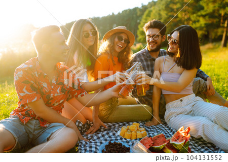 Group of happy friends cheers, drink beers on in summer park. Vacation, picnic holliday concept. 104131552