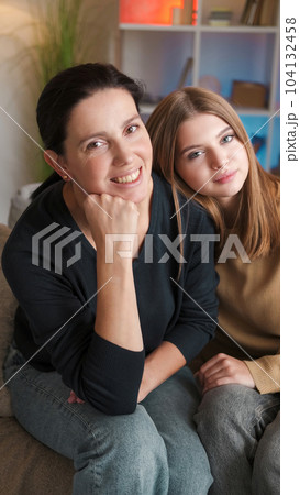 Family portrait. Happy relationship. Smiling mother teenage daughter enjoying spending time together sitting couch in light home interior. 104132458