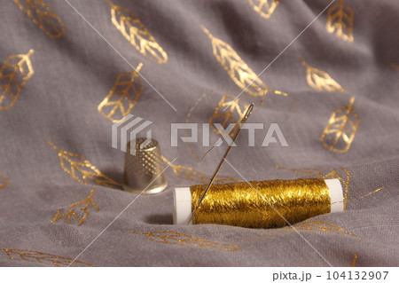 Spool of Metallic Gold Thread on Gray and Gold Fabric 104132907