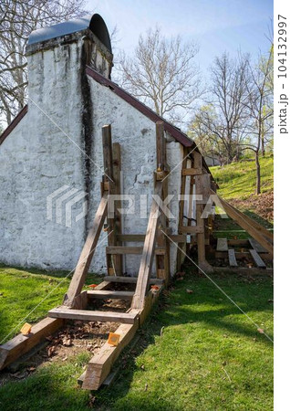 Wooden support scaffolding braces cracked wall of colonial cottage 104132997