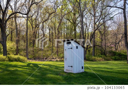 White colonial Pennsylvania outhouse in grass field with tall trees White colonial Pennsylvania outhouse in grass field with tall trees 104133065