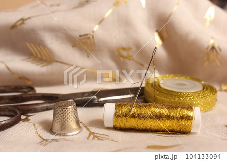 Spool of Gold Thread and Scissors With Thimble on Metallic Fabric Spool of Gold Thread and Scissors With Thimble on Metallic Fabric 104133094