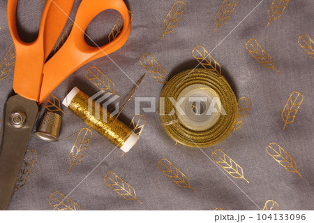 Spool of Metallic Gold Thread on Gray and Gold Chiffon Fabric 104133096
