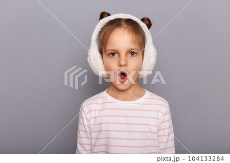 Indoor shot of shocked amazed surprised little girl standing and looking at camera with open mouth, sees something astonishing, hearing breaking news. 104133284