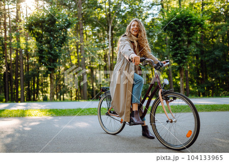 Young happy woman rides bicycle in sunny park. Beautiful woman enjoys autumn nature. Lifestyle. Young happy woman rides bicycle in sunny park. Beautiful woman enjoys autumn nature. Lifestyle. 104133965