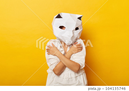 Horizontal shot of selfish anonymous woman wearing dress and paper cat mask hugging herself, expressing love and care to herself, posing isolated over yellow background. Horizontal shot of selfish anonymous woman wearing dress and paper cat mask hugging herself, expressing love and care to herself, posing isolated over yellow background. 104135746