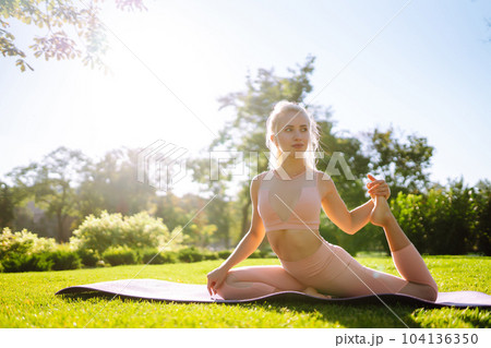 Pretty woman doing yoga exercises in the park. Portrait of woman in sportswear practicing yoga at nature. 104136350