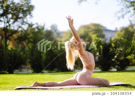 Pretty woman doing yoga exercises in the park. Portrait of woman in sportswear practicing yoga at nature. Pretty woman doing yoga exercises in the park. Portrait of woman in sportswear practicing yoga at nature. 104136354