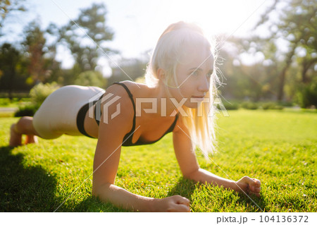 Pretty woman doing yoga exercises in the park. Portrait of woman in sportswear practicing yoga at nature. 104136372