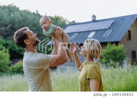 Happy family near their house with solar panels. Alternative energy, saving resources and sustainable lifestyle concept. Happy family near their house with solar panels. Alternative energy, saving resources and sustainable lifestyle concept. 104136852