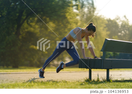Full lenght portrait of beautiful fitness woman doing mountain clibers exercise against park bench. Full lenght portrait of beautiful fitness woman doing mountain clibers exercise against park bench. 104136953