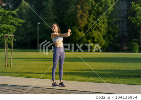 Full lenght portrait of beautiful fitness woman stretching before outdoor workout in the city park. 104136954
