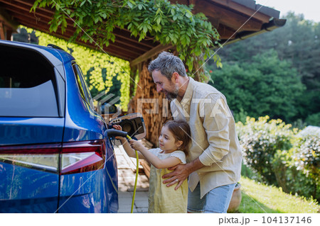 Father with his little daughter charging their electric car. 104137146