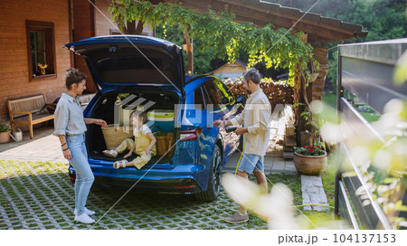 Father charging their electric car, little daughter and mother waiting in a car trunk. 104137153