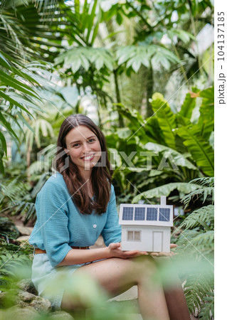 Young woman in jungle holding paper model of house with solar panels, concept of renewable energy and protection of nature. 104137185