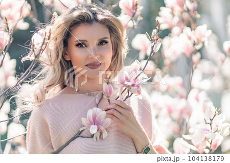 Portrait of a beautiful happy middle aged woman enjoying the smell in a blooming spring garden. Beautiful magnolia bushes, large flowers. Portrait of a beautiful happy middle aged woman enjoying the smell in a blooming spring garden. Beautiful magnolia bushes, large flowers. 104138179