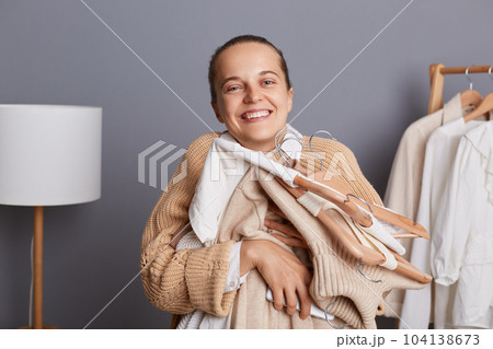 Portrait of young adult woman shopper holding clothes on racks in modern boutique, embracing her new attires, being happy to do shopping, enjoying her new clothing, buying outfits in showroom. Portrait of young adult woman shopper holding clothes on racks in modern boutique, embracing her new attires, being happy to do shopping, enjoying her new clothing, buying outfits in showroom. 104138673