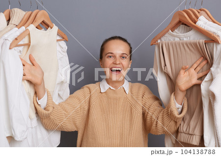 Image of extremely happy positive optimistic woman stylist standing near clothes hang on shelf, screaming with raised arms, selling many attires and celebrating her success. 104138788