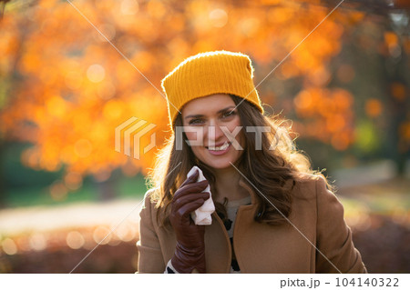 smiling stylish woman in beige coat and orange hat 104140322