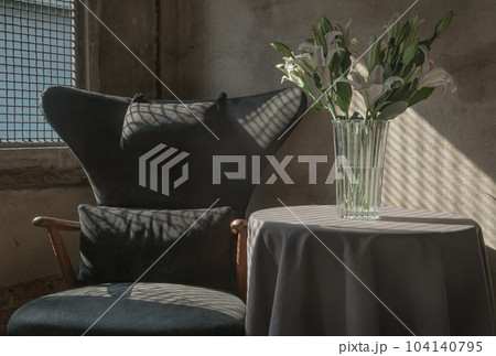 A Wooden Upholstered Chair and the Bouquet of Flowers in a Glass Vase on Table in the Room with Bare Cement Wall. 104140795