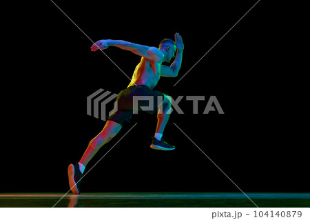 Young man with fit, muscular, relief body shape, professional sportsman in motion, running against black studio background in neon light 104140879