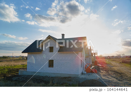 Aerial view of unfinished house with aerated lightweight concrete walls and wooden roof frame covered with metallic tiles under construction. Aerial view of unfinished house with aerated lightweight concrete walls and wooden roof frame covered with metallic tiles under construction. 104144641