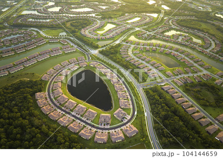 Aerial view of tightly packed homes in Florida closed living clubs with lake water in the middle. Family houses as example of real estate development in american suburbs 104144659
