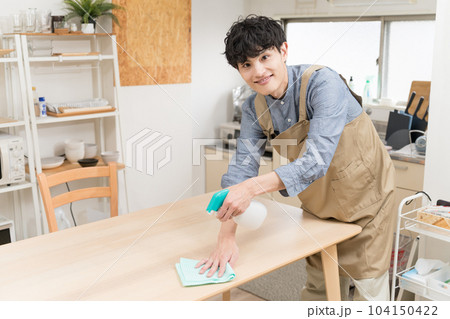 キッチンダイニングでテーブルを拭いている若い男性 104150422