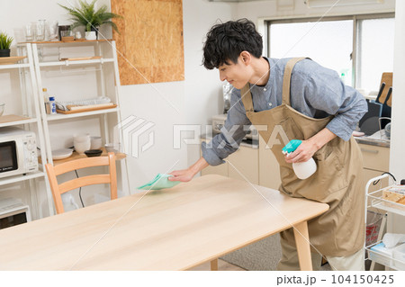 キッチンダイニングでテーブルを拭いている若い男性 104150425