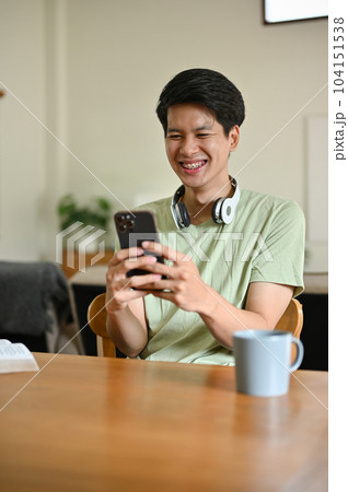 A cheerful young Asian man enjoys chatting with his friends through his smartphone 104151538