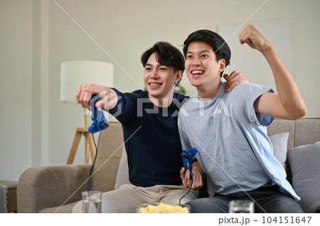 Two overjoyed Asian male friends celebrated their game wins while playing video games together. Two overjoyed Asian male friends celebrated their game wins while playing video games together. 104151647