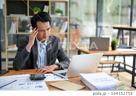 A stressed and thoughtful Asian businessman is working at his desk in the office. 104152758