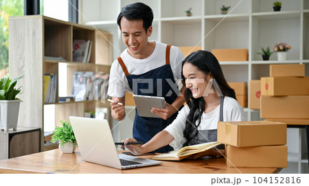 A cheerful online seller couple is looking down at a laptop screen, excited with their online orders A cheerful online seller couple is looking down at a laptop screen, excited with their online orders 104152816