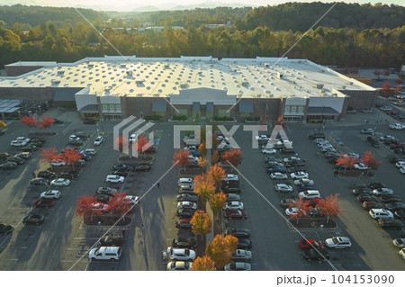 Aerial view of large parking lot in front of rgocery store with many parked colorful cars. Carpark at supercenter shopping mall with lines and markings for vehicle places and directions 104153090