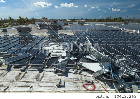Aerial view of damaged by hurricane wind photovoltaic solar panels mounted on industrial building roof for producing green ecological electricity. Consequences of natural disaster 104153265