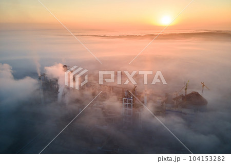 Aerial view of cement factory with high concrete plant structure and tower crane at industrial production site on foggy morning. Manufacture and global industry concept. 104153282