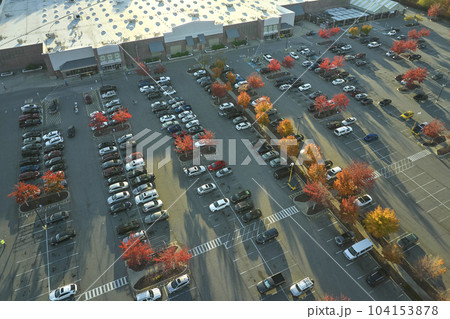 Aerial view grocery shopping mall and many colorful cars parked on parking lot with lines and markings for parking places and directions. Place for vehicles in front of a strip mall plaza Aerial view grocery shopping mall and many colorful cars parked on parking lot with lines and markings for parking places and directions. Place for vehicles in front of a strip mall plaza 104153878