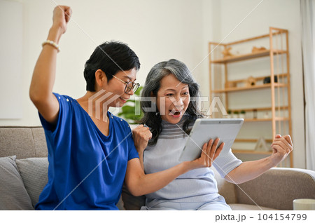 Two overjoyed retired middle-aged female besties are watching a lottery drawing online together 104154799