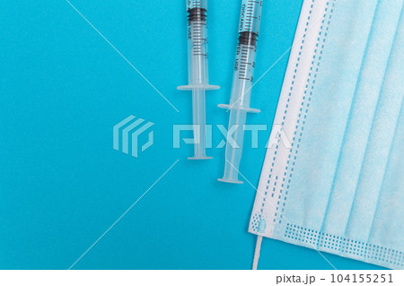 Syringe with Medical Mask on Blue Table - Flat Lay Syringe with Medical Mask on Blue Table - Flat Lay 104155251