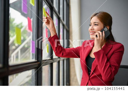 A confident businesswoman is talking on the phone while standing and looking out the window. 104155441
