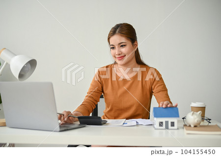 A beautiful Asian female real estate agent working at her desk, using her laptop 104155450