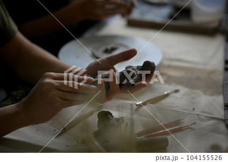 A man in a clay sculpture workshop, molding raw clay to make an ornament at a table in the studio. A man in a clay sculpture workshop, molding raw clay to make an ornament at a table in the studio. 104155526