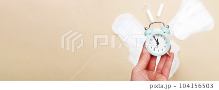 Women's hygiene pads with tampons and alarm clock on beige background 104156503