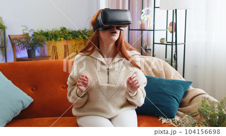Woman using virtual reality futuristic technology headset to play simulation 3D video game at home 104156698
