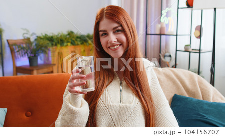 Thirsty young woman sitting at home holding glass of natural aqua make sips drinking still water 104156707