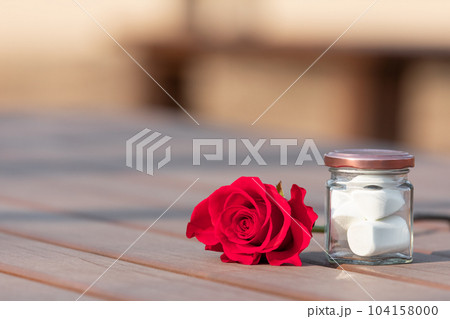 White marshmallows in a glass jar and a red rose next to them. White marshmallows in a glass jar and a red rose next to them. 104158000