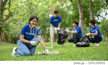 A smiling Asian female volunteer is helping her team clean up an area in a public park. A smiling Asian female volunteer is helping her team clean up an area in a public park. 104158092
