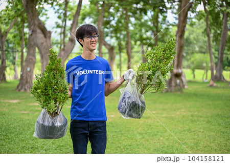 A happy Asian male volunteer walks with plants in his hands, gardening for their community park. 104158121