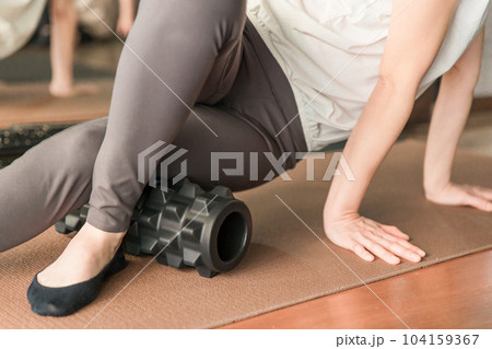 ジムでフォームローラーを使って太ももの筋膜リリースをする女性 104159367